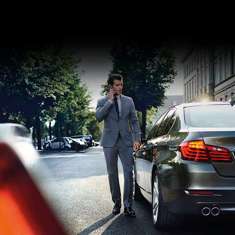 BMW driver in grey suit reporting an incident on the phone standing next to his BMW