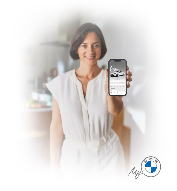 A woman in a white jumpsuit holding up a smartphone to show the My BMW App in action