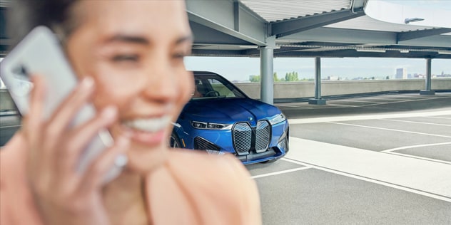 A smiling woman talks on her smartphone after parking her BMW iX xDrive50