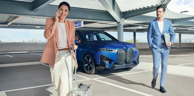 A couple in business attire walks away from their BMW in a parking garage