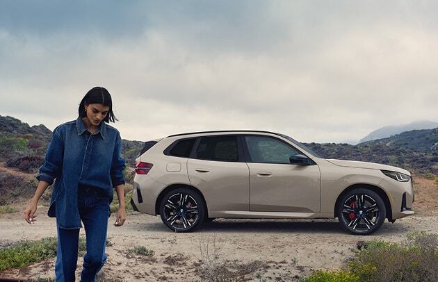 A woman walks away from her BMW X3 M50 xDrive in a scenic desert setting.