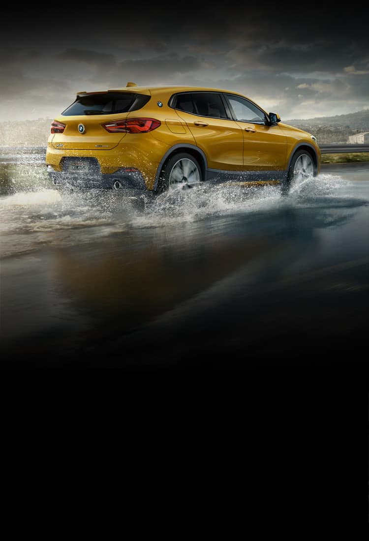 A BMW X2 driving smoothly on a slightly flooded street with mountainous landscrape background.