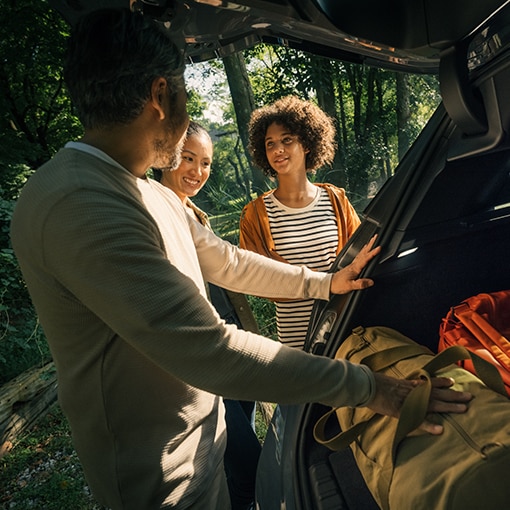 A man and two women at the rear of a BMW iX, smiling and placing luggage into the cargo area.