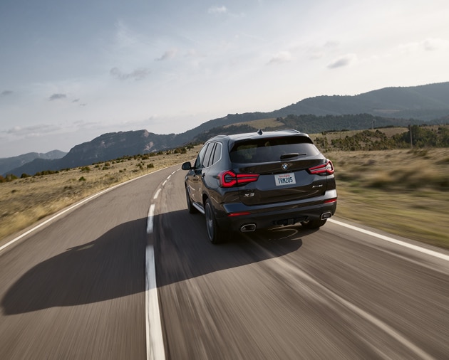 A BMW X3 SUV driving along a road through open countryside