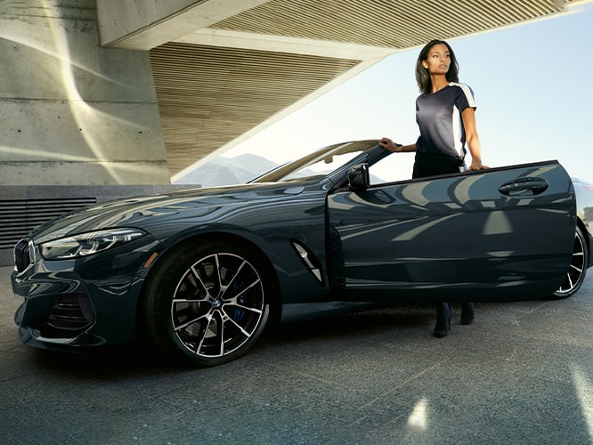 An impeccably dressed female BMW driver opens the door of her 2026 BMW 840i Convertible