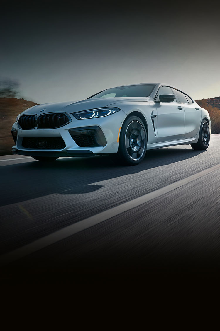 2025 BMW M8 Competition Gran Coupe speeds down a road with blurred scenery in the background