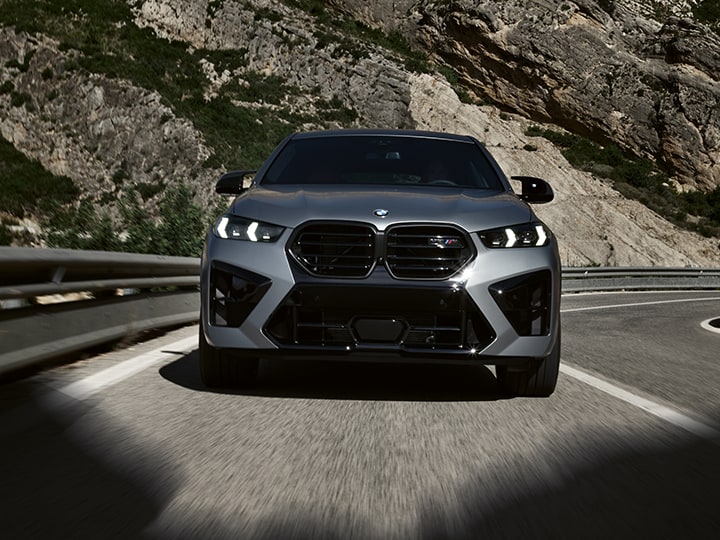 Front view of 2026 BMW X6 M Competition driving on a rural highway