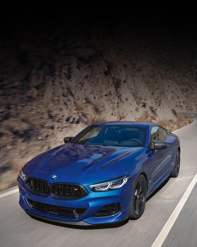 The 2026 BMW M850i xDrive Coupe driving down a canyon road