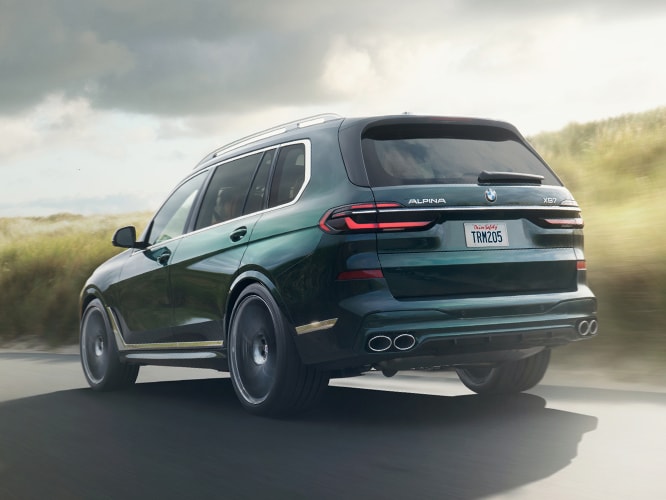 A 2026 ALPINA XB7 accelerates down a road between grass-covered dunes