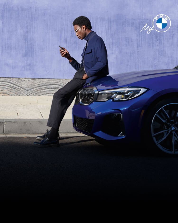BMW driver exploring app while sitting on the hood of his BMW